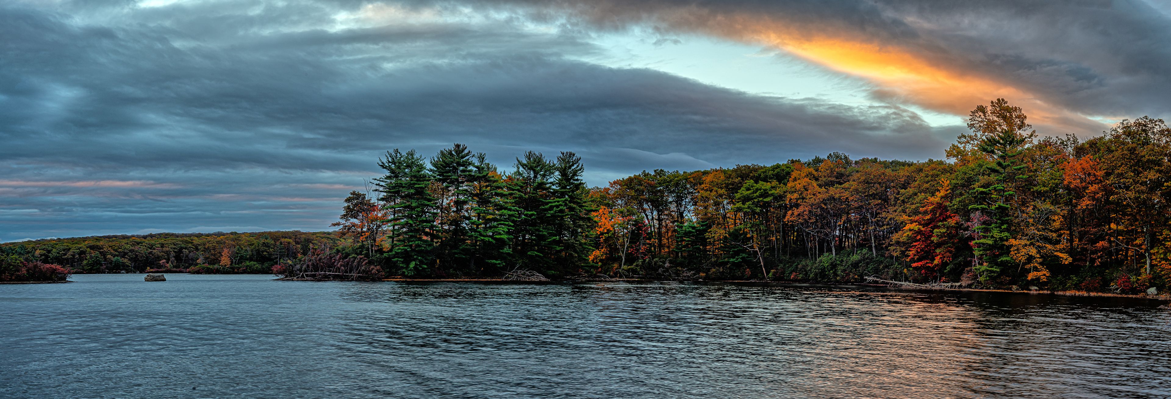A lake surrounded by autumn-colored trees under a cloudy sky.