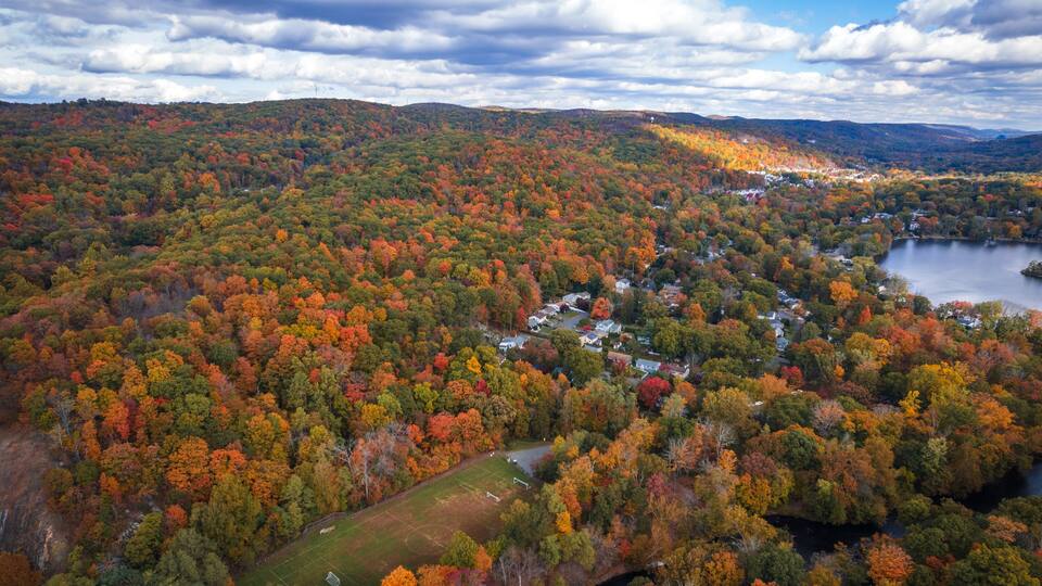 A mountainous landscape with autumn foliage, a lake, and a residential area.