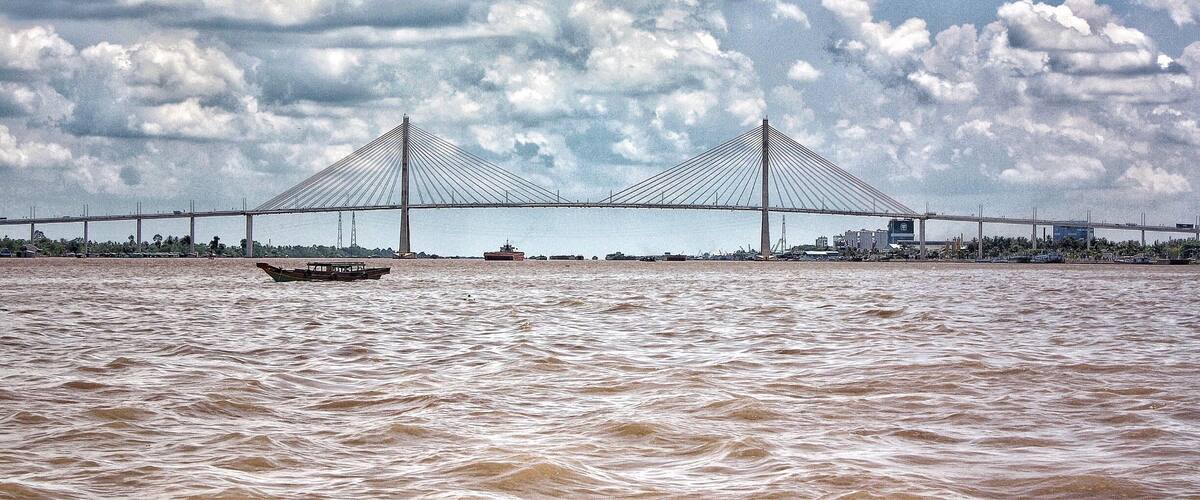 A large suspension bridge over a river with a boat in the foreground.