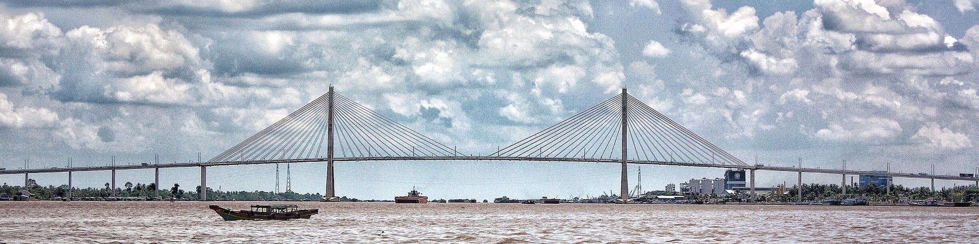 A large suspension bridge over a river with a boat in the foreground.