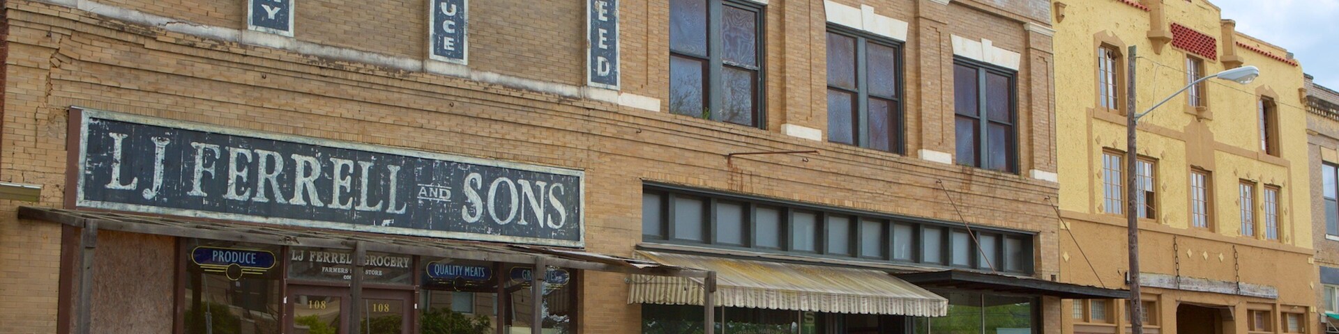 Una calle con un edificio que dice "L J Ferrell and Sons" y otro edificio con un letrero de "Produce".
