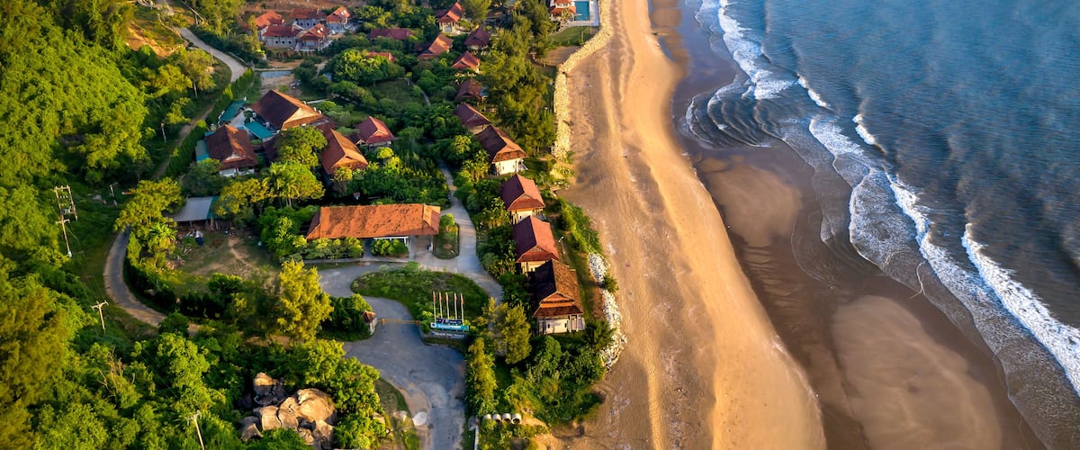 An aerial view of a coastal village with houses, a beach, and dense greenery.