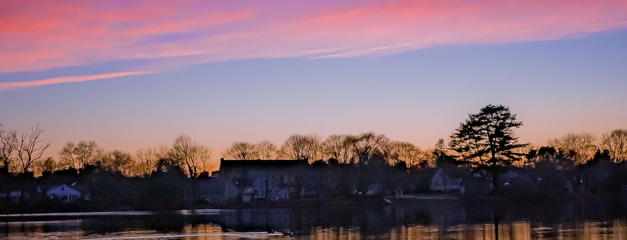 Un lago tranquilo que refleja un cielo de atardecer con tonos morados y rosados.