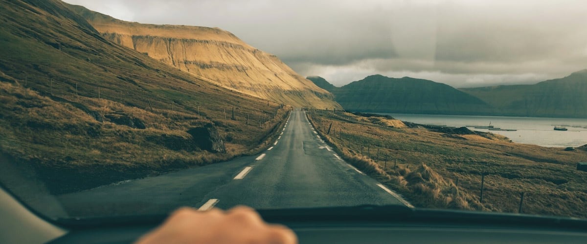 A road leading through a hilly landscape with a body of water in the distance.