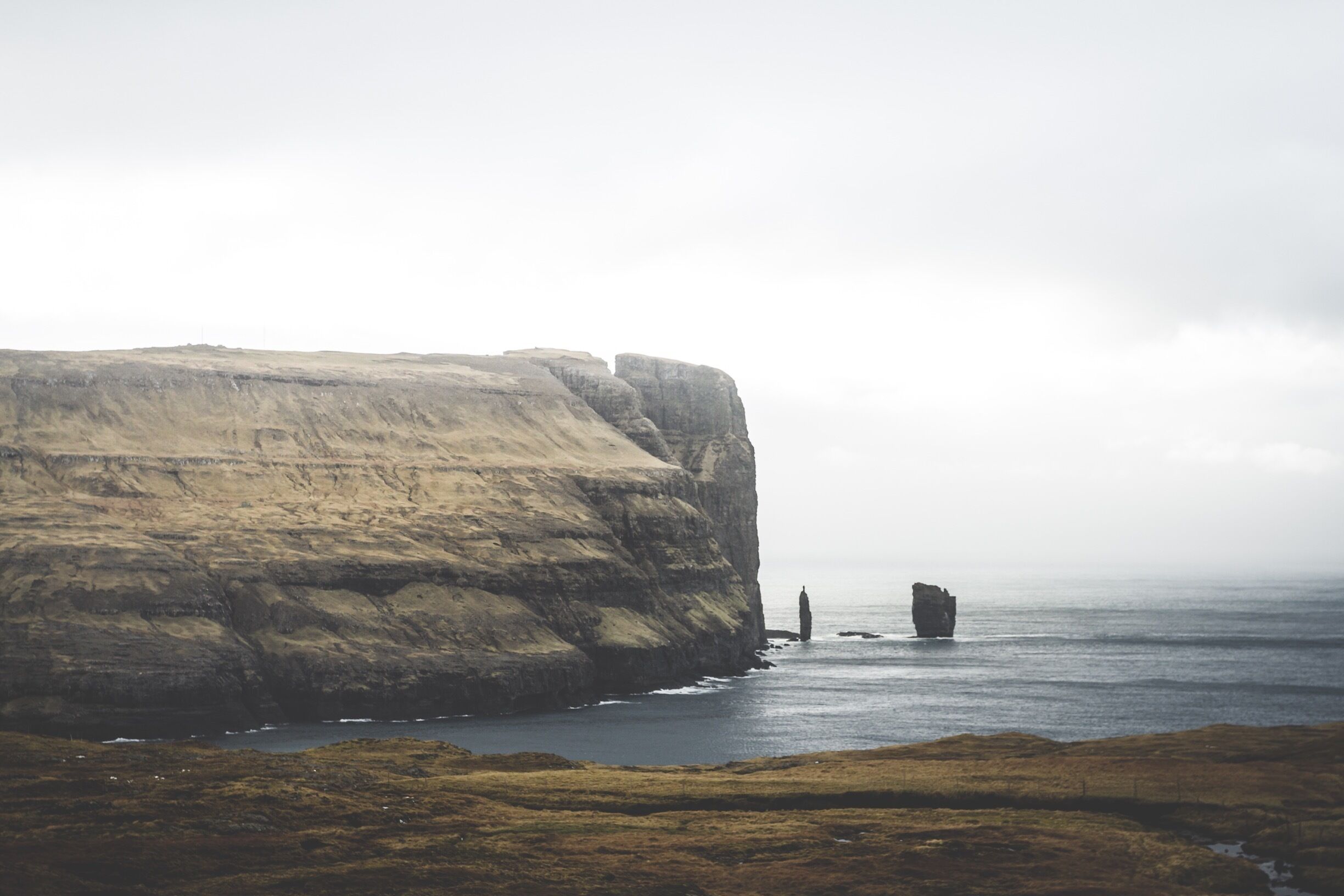 A coastal cliff with a rocky outcrop in the sea.