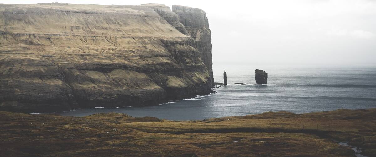 A coastal cliff with a rocky outcrop in the sea.