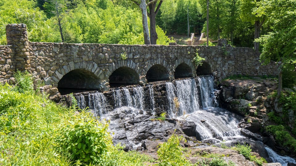 A stone bridge with three arches over a cascading waterfall surrounded by lush greenery.