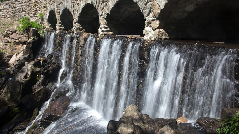 A waterfall cascading over rocks with a stone bridge in the background.
