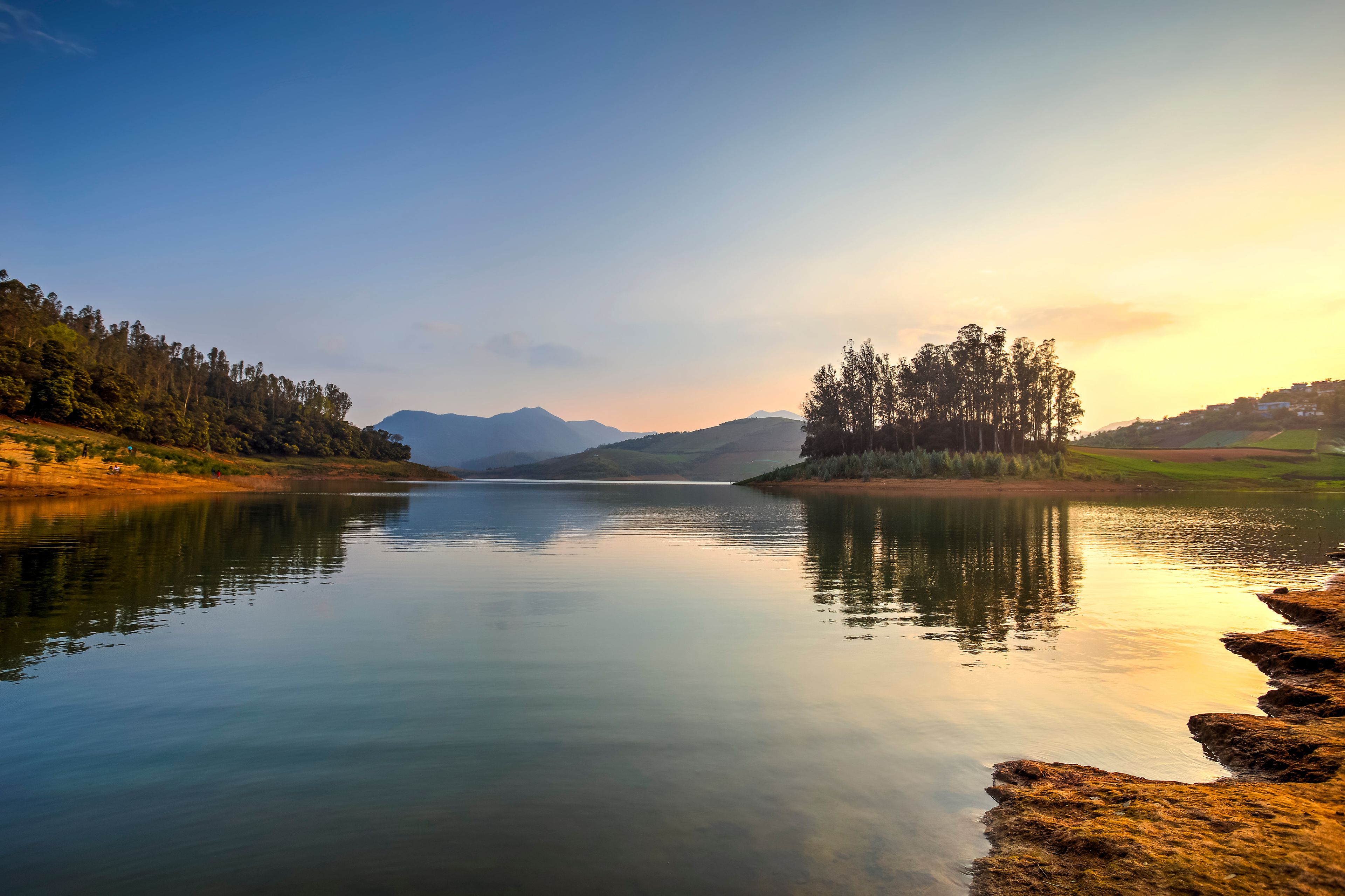 A calm lake with mountains in the background, surrounded by dense forests and a clear sky.