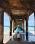 A person standing under a pier with a view of the ocean.