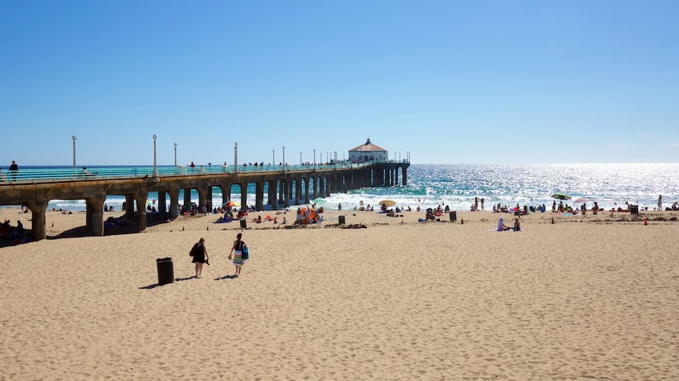 A beach with a pier extending into the ocean, people sunbathing, and umbrellas on the sand.