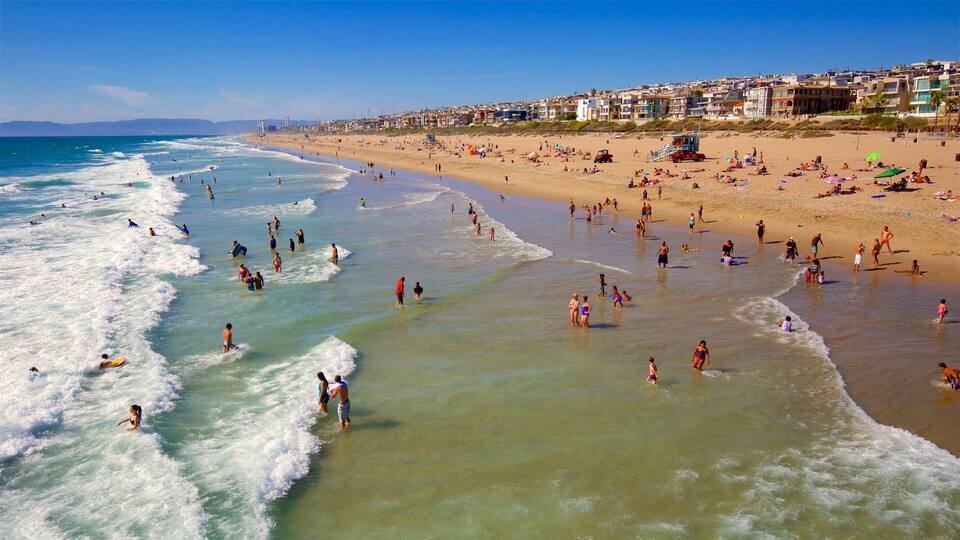 A crowded beach with people swimming and sunbathing, and buildings in the background.