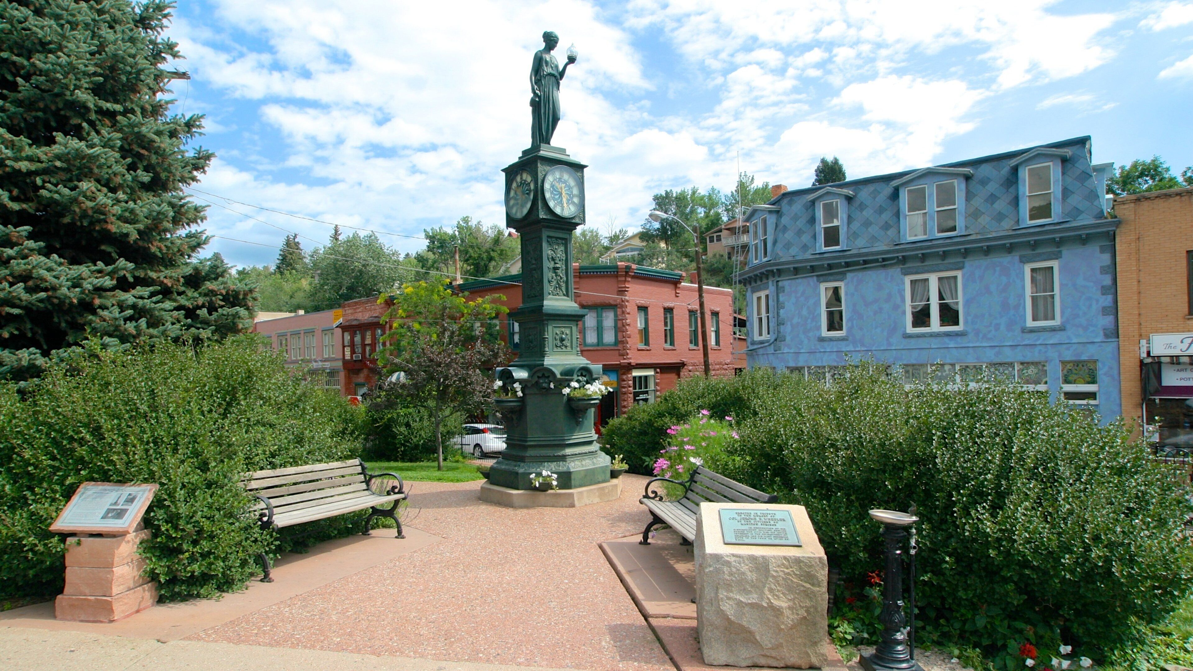 A park with a clock tower, benches, and historic buildings.