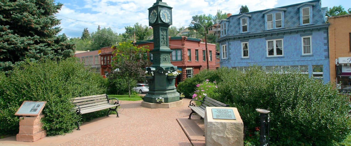 A park with a clock tower, benches, and historic buildings.