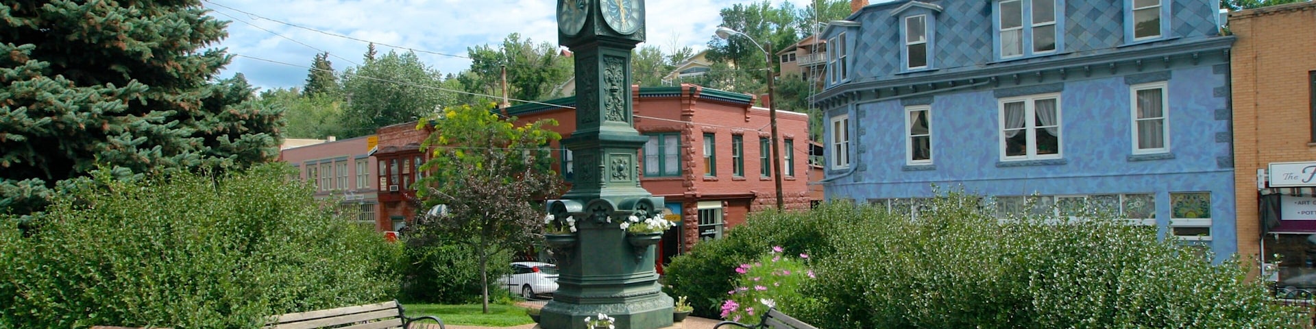 A park with a clock tower, benches, and historic buildings.