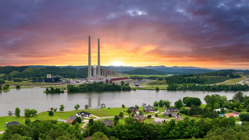 A power plant with cooling towers and a large body of water surrounded by greenery and residential areas.