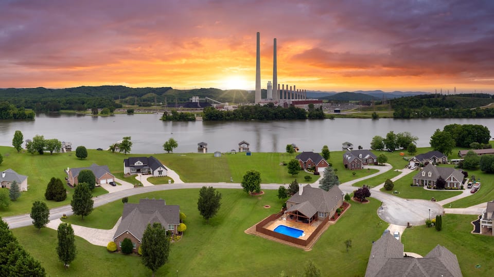 A residential area with houses, a swimming pool, and a large industrial facility with tall chimneys.