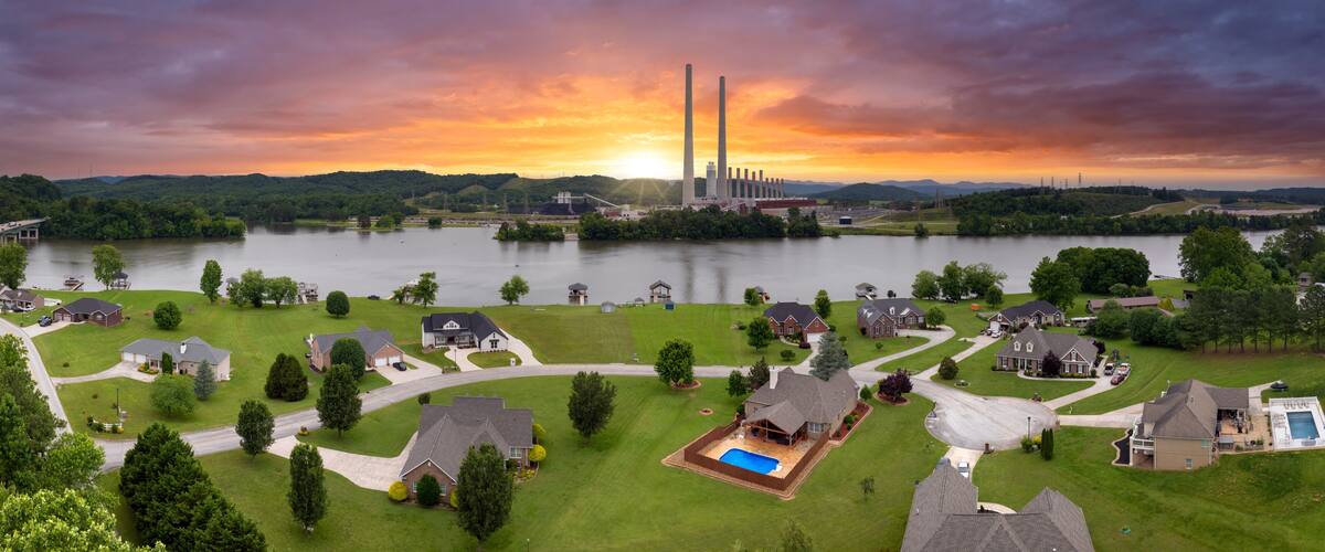 A residential area with houses, a swimming pool, and a large industrial facility with tall chimneys.