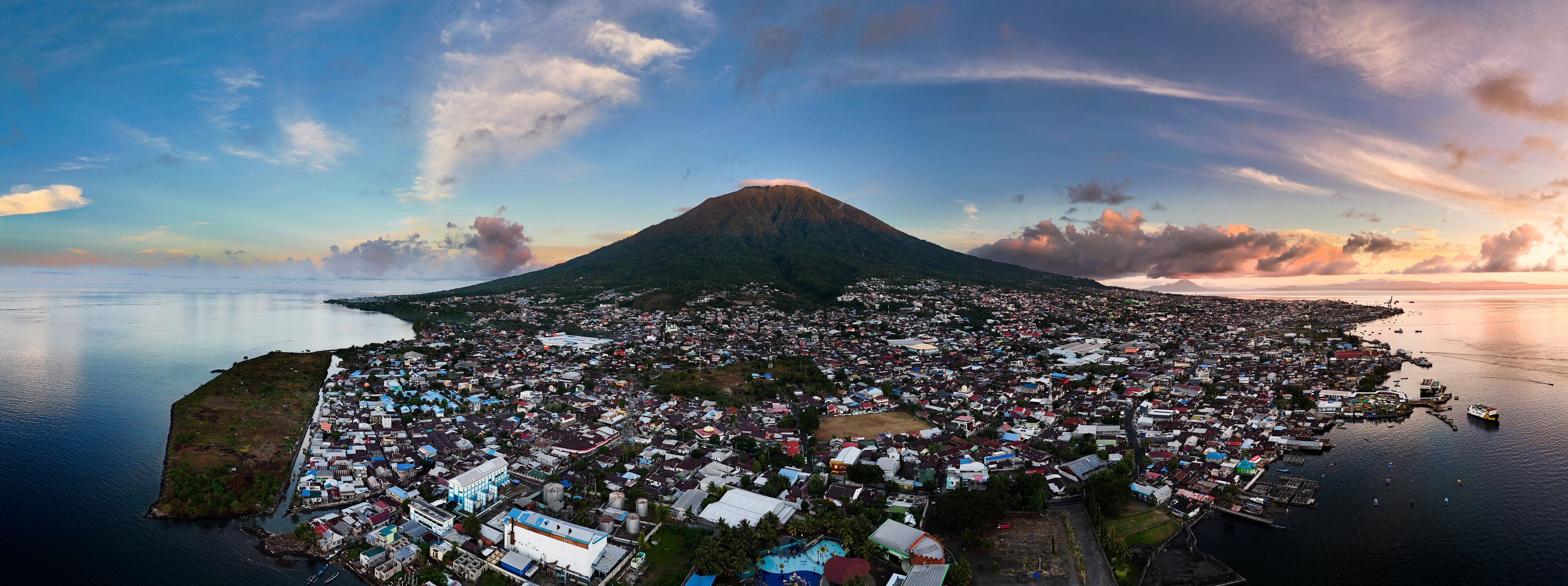 An aerial view of a coastal town with a prominent volcano in the background.