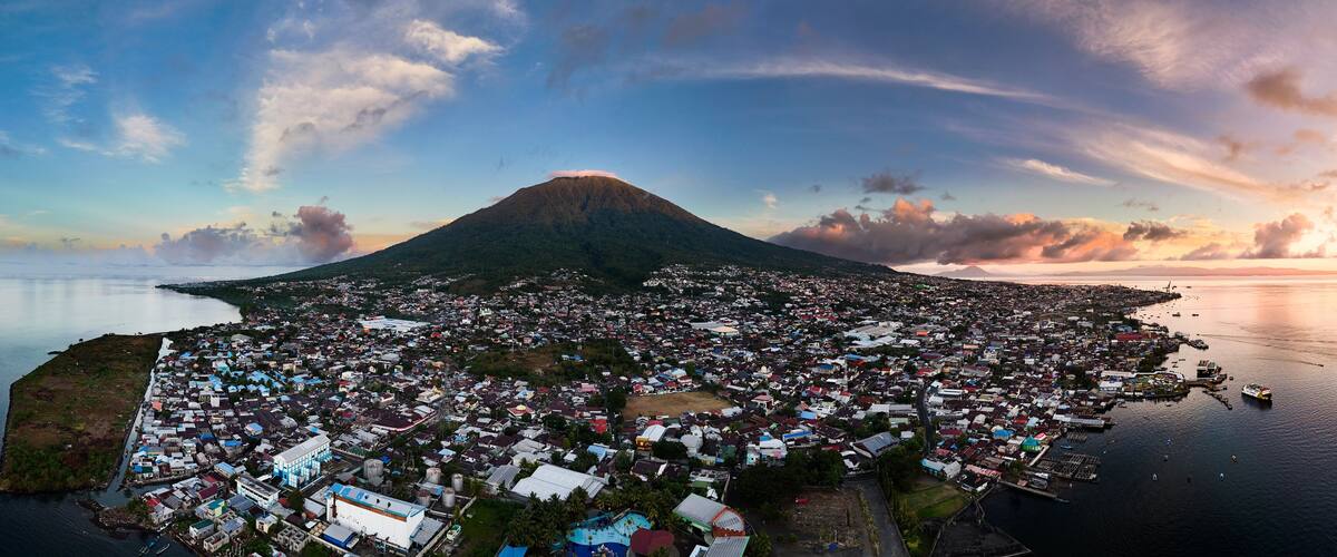 An aerial view of a coastal town with a prominent volcano in the background.