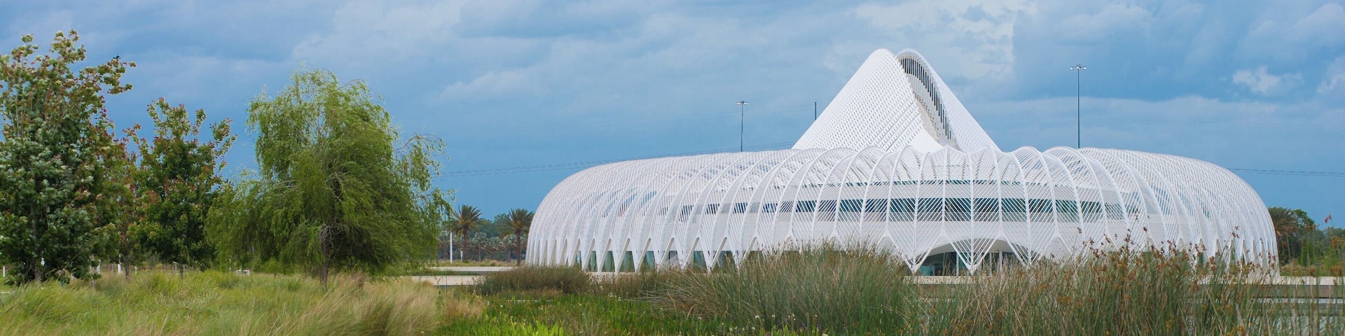 #Details
The Innovation, Science, and Technology (IST) Building is Florida Poly’s flagship building and the main classroom and laboratory building. The 162,000-square-foot, white-domed building is a moveable and functional work of art, with a louvered roof system that moves throughout the day providing passive lighting inside the second-floor atrium. The oval-shaped building is ringed by curved metal pergolas that shade its outer terrace and walkways.