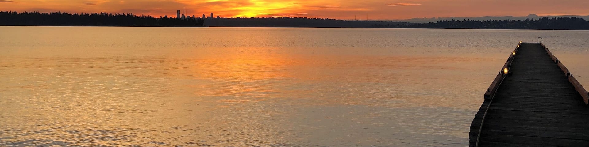 A sunset over a calm lake with a wooden pier extending into the water.