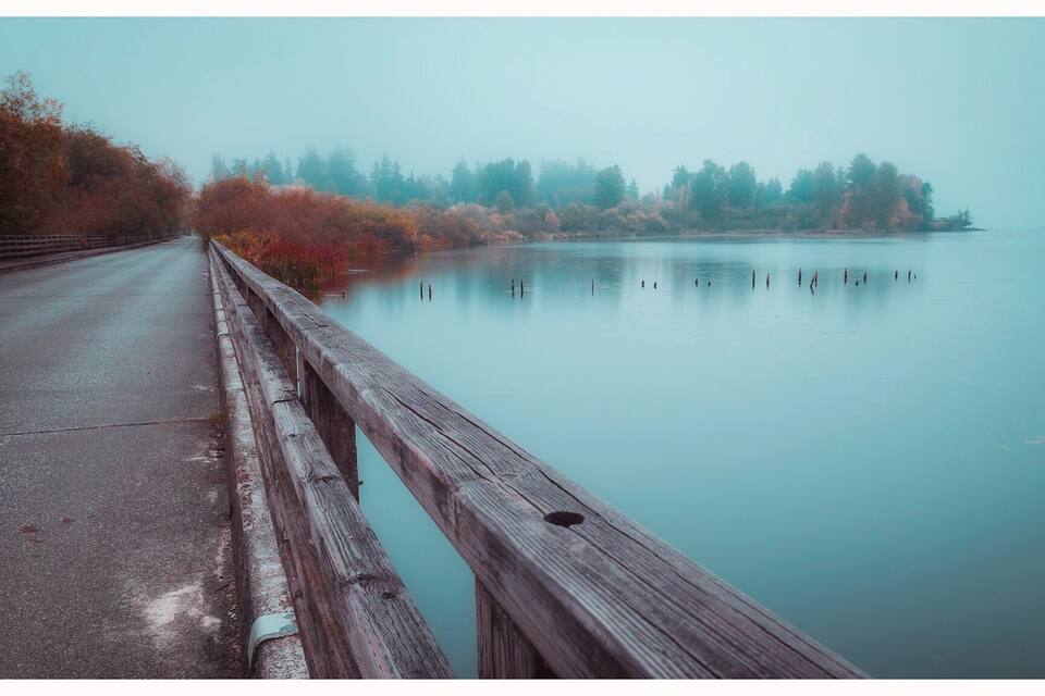 A wooden bridge over a calm lake with autumn foliage on the banks.
