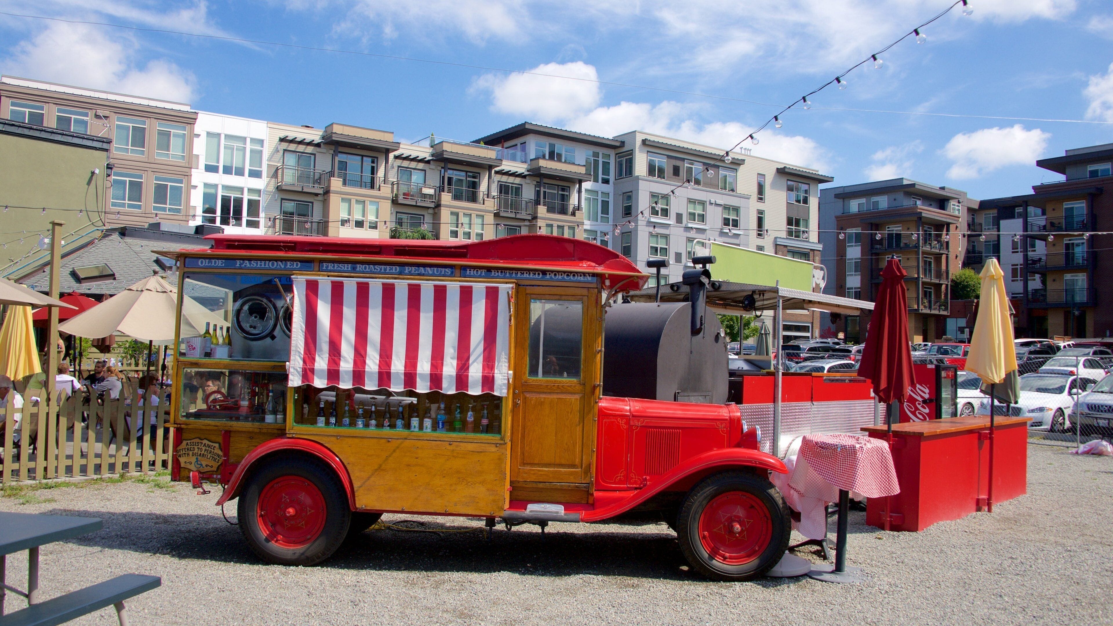 A vintage red and yellow food truck parked on a street with modern buildings in the background.