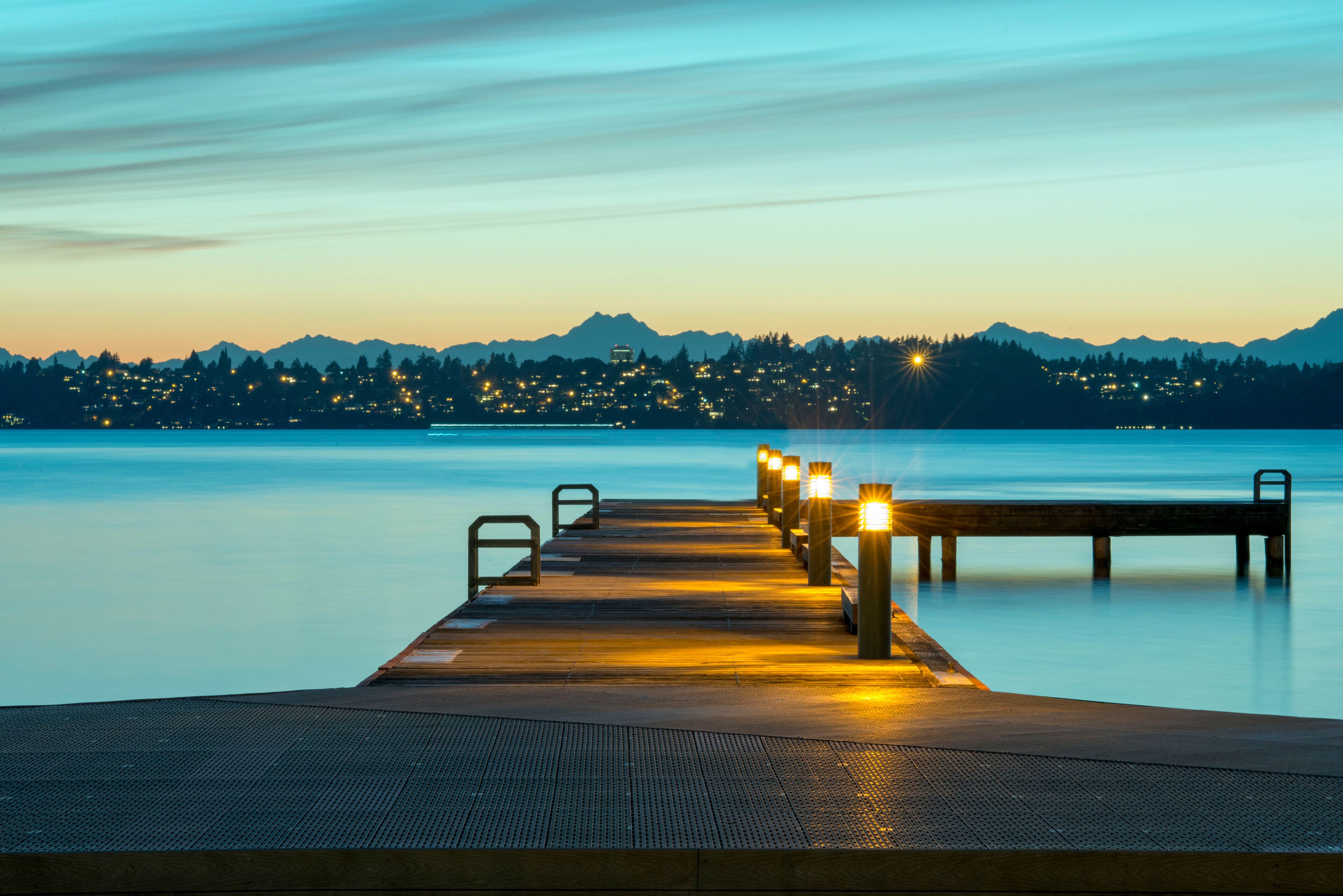 A wooden pier extending into calm waters with city lights in the background.