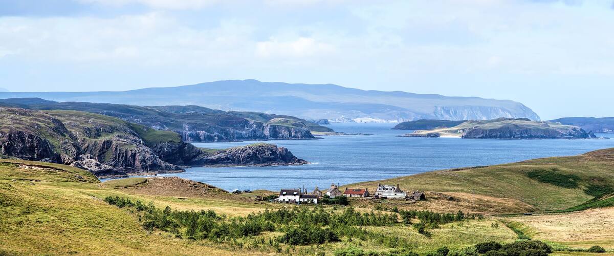 A coastal landscape with rugged cliffs, a small settlement, and a clear view of the sea.