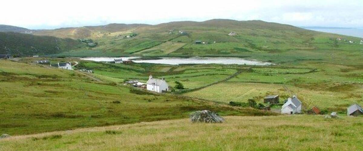 Rolling hills, a small body of water, and scattered houses in a rural landscape.