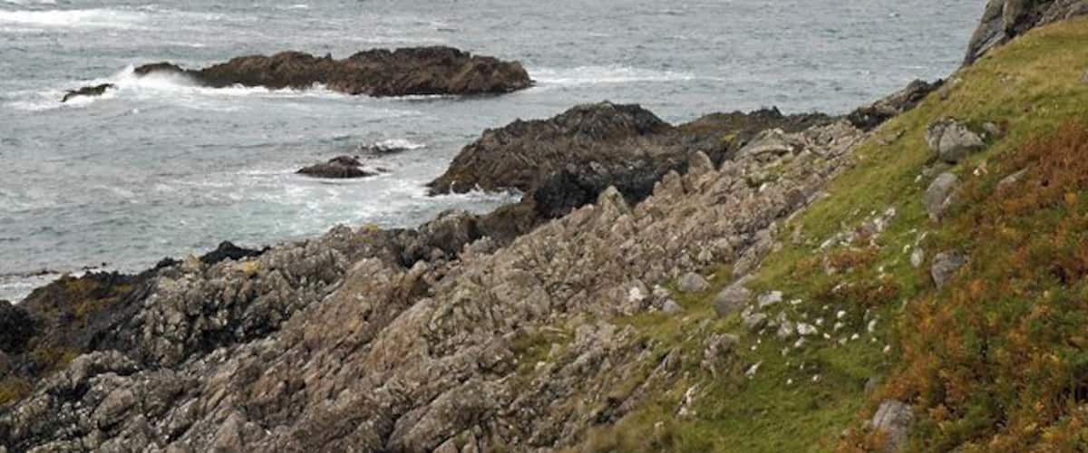 A rocky coastline with waves crashing against rocks and a grassy cliff.