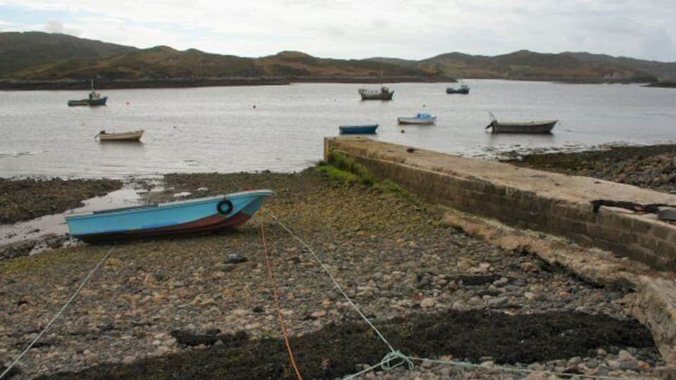 A rocky shoreline with several boats anchored in the water and a distant hilly landscape.