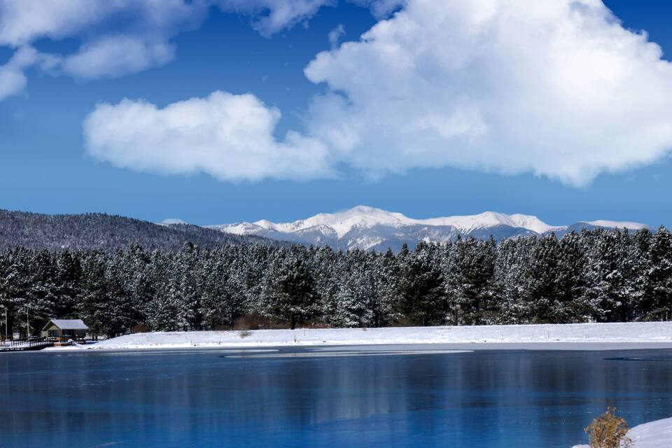 A frozen lake with snow-covered trees and mountains in the background.