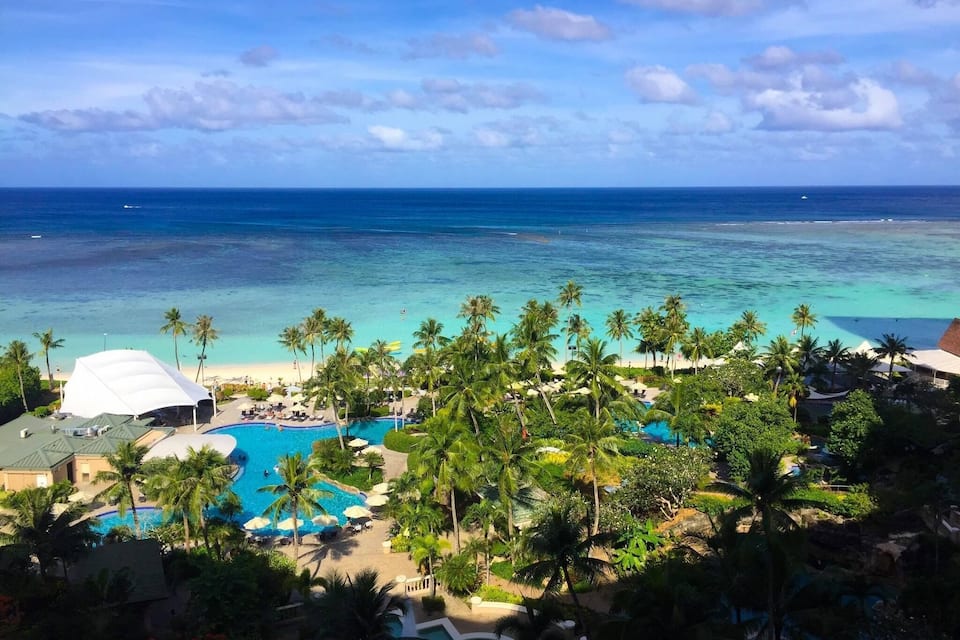 A resort with a pool, palm trees, and a beach.