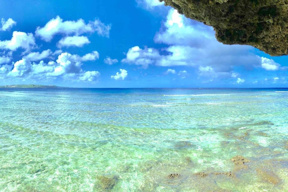 A clear blue sea with shallow waters and a rocky overhang.