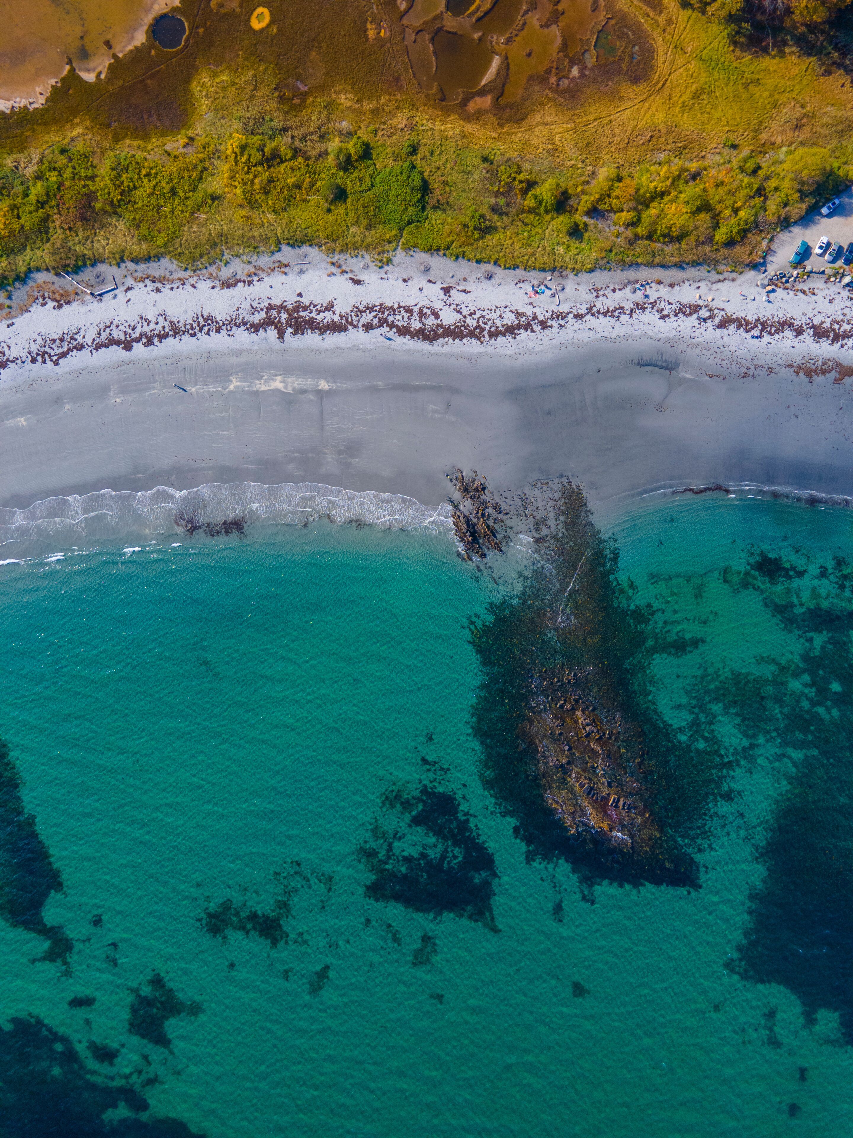 An aerial view of a beach with clear turquoise waters, a sandy shore, and a large submerged structure.