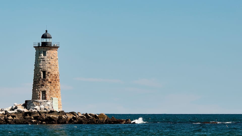 A lighthouse on a rocky shore with the ocean in the background.