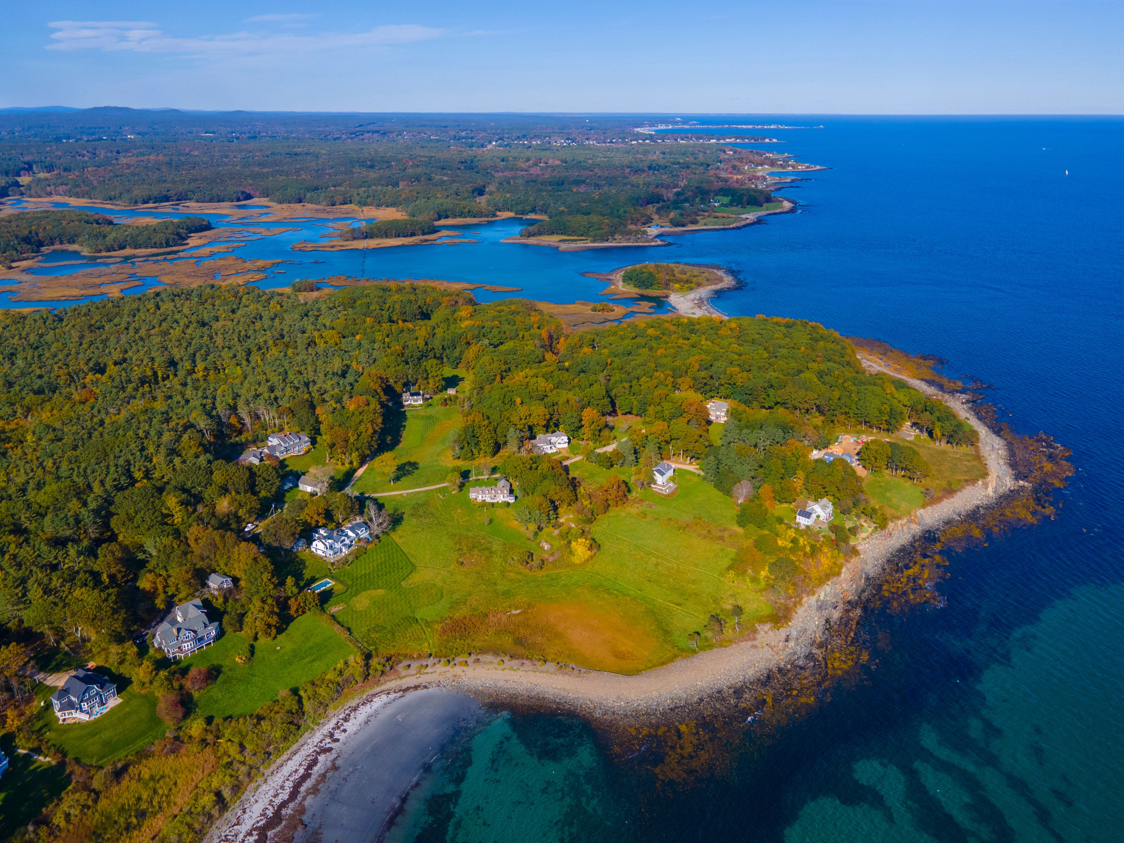 An aerial view of a coastal area with a mix of forested land and residential properties.