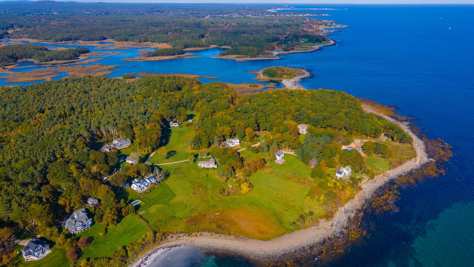 An aerial view of a coastal area with a mix of forested land and residential properties.