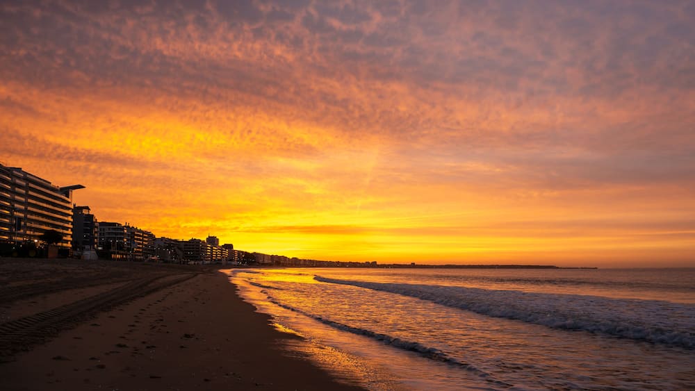 Amazing view of a fiery sunrise with multicolored clouds. Sea waves along the seashore at sunrise. Morning time. Ocean view. La Baule-Escoublac, France