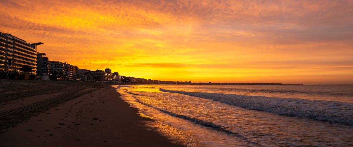 Amazing view of a fiery sunrise with multicolored clouds. Sea waves along the seashore at sunrise. Morning time. Ocean view. La Baule-Escoublac, France