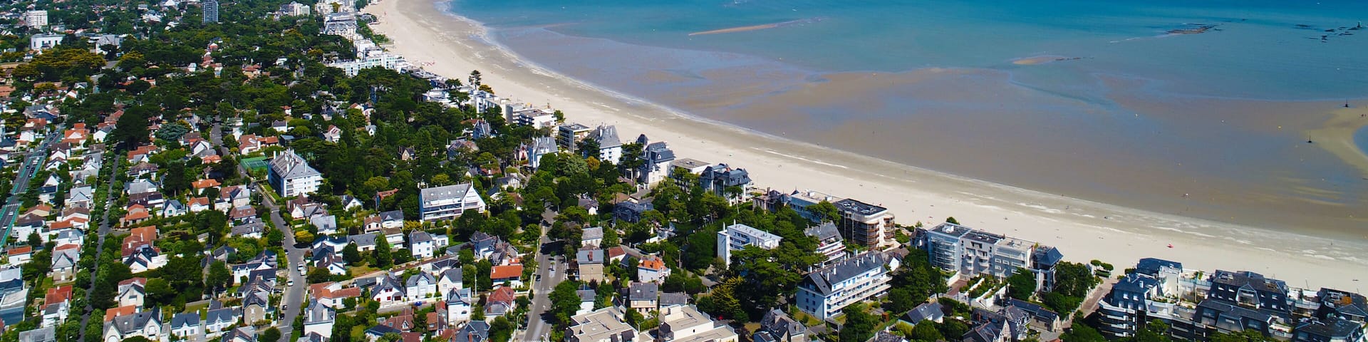A coastal cityscape with a wide beach, dense residential area, and clear blue skies.