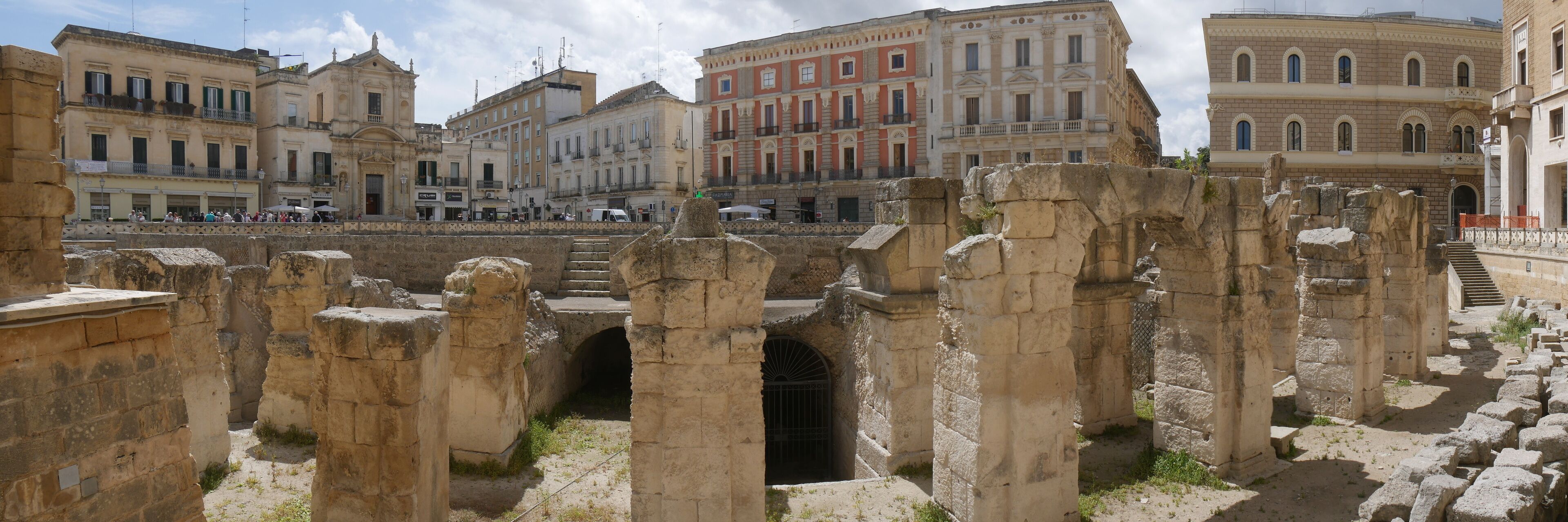 Ancient ruins with stone columns and arches, surrounded by historic buildings.
