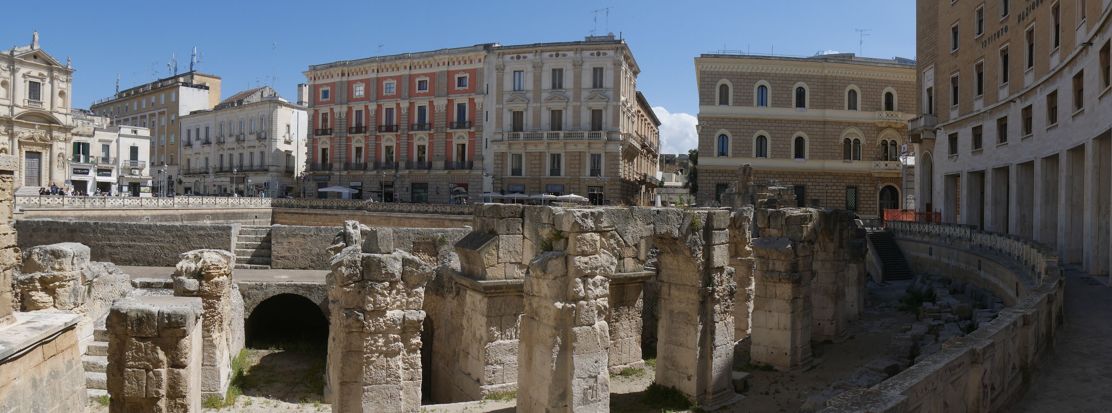 Ancient ruins with stone columns and arches, surrounded by historic buildings.