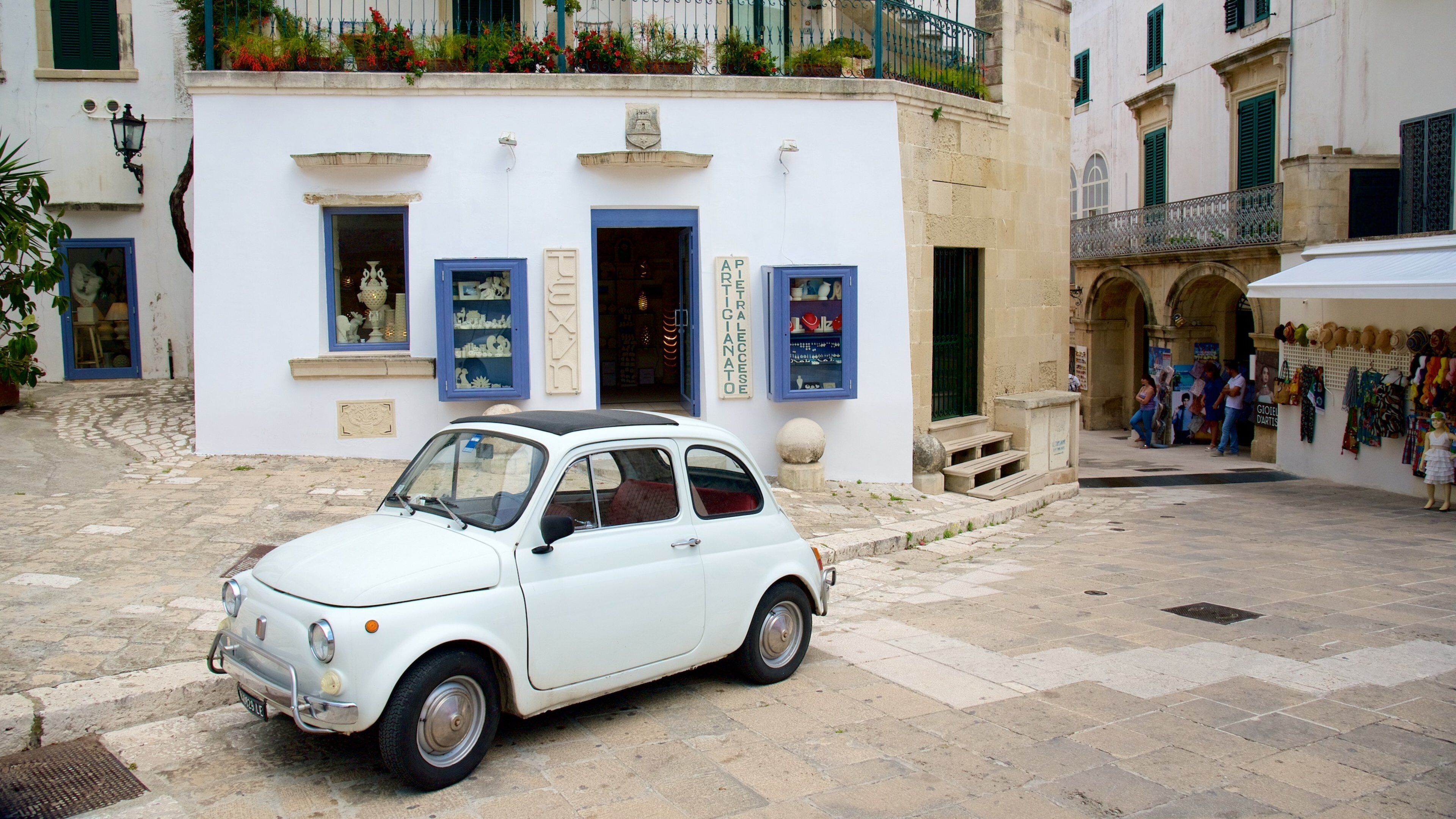 A white vintage car parked in front of a white building with blue shutters and a sign that reads "PIETRALECCIATO".