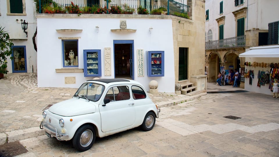 A white vintage car parked in front of a white building with blue shutters and a sign that reads "PIETRALECCIATO".
