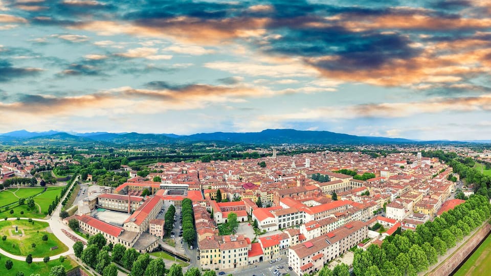 A panoramic view of a city with a historic fortress, surrounded by mountains and a river.