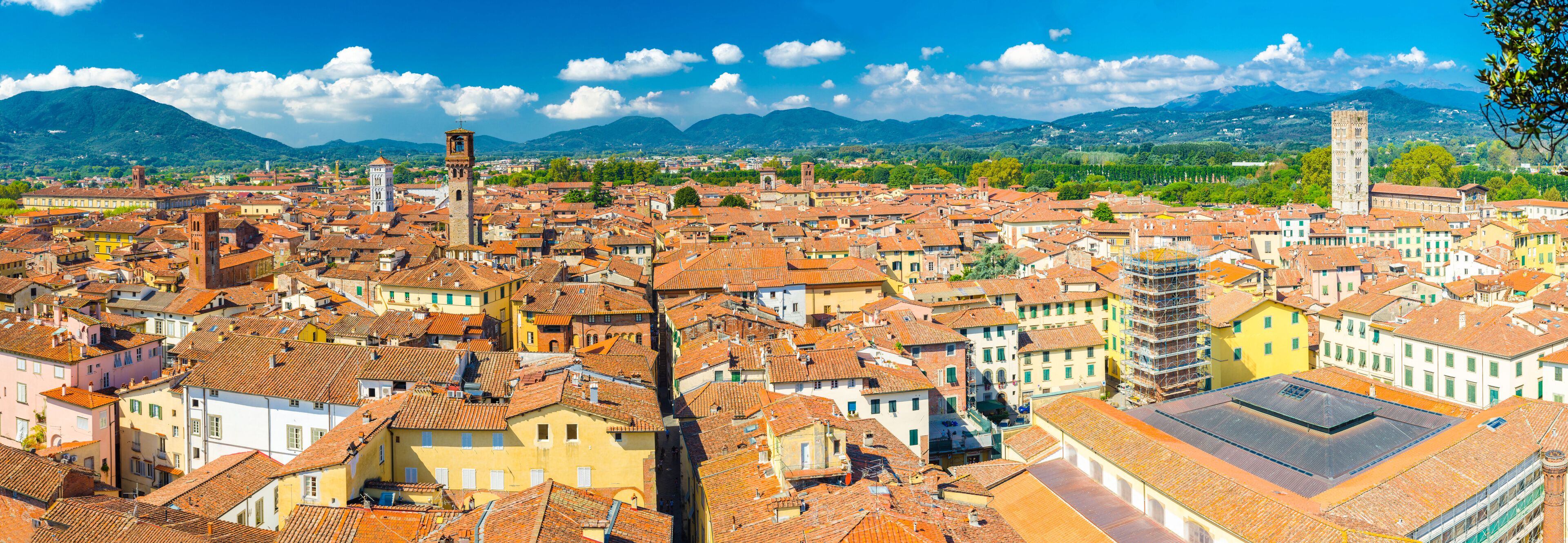 Aerial top panoramic view of historical centre medieval town Lucca with old buildings, typical orange terracotta tiled roofs and mountain range, hills, blue sky white clouds background, Tuscany, Italy