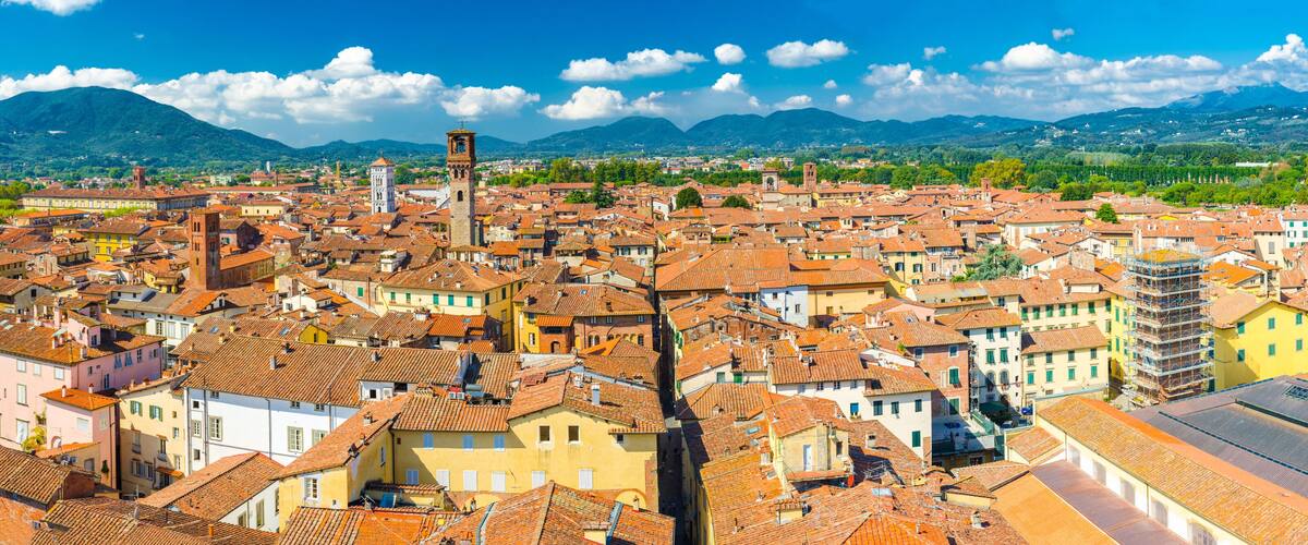 Aerial top panoramic view of historical centre medieval town Lucca with old buildings, typical orange terracotta tiled roofs and mountain range, hills, blue sky white clouds background, Tuscany, Italy